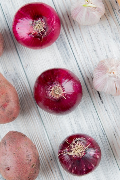 Free photo close up view of pattern of vegetables as red onion potato garlic on wooden background