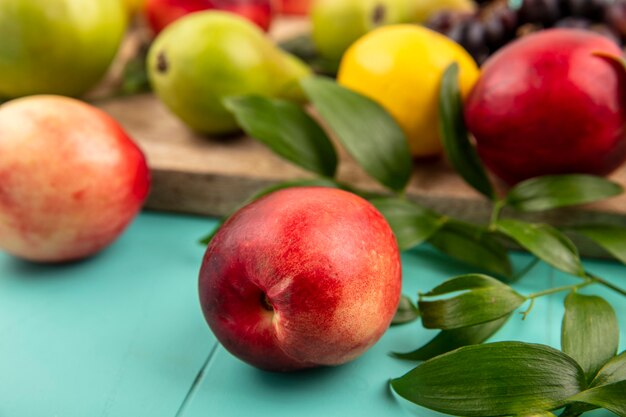 Close-up view of peach with leaves and pear lemon on cutting board on blue background