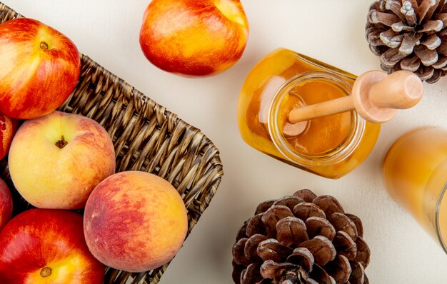Close-up view of peaches and glass jar of plum jam and juice with pinecones on white table