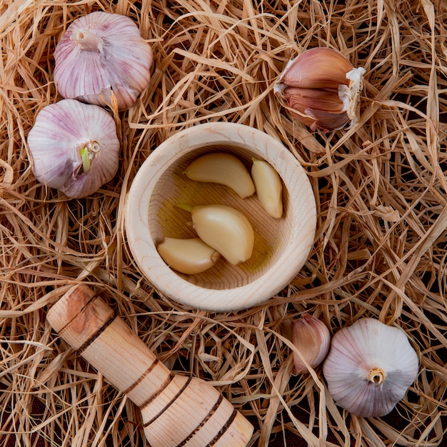 Close-up view of peeled garlic cloves in garlic crusher and garlic bulbs on straw background