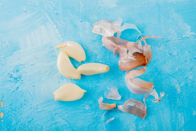 Close-up view of peeled garlic cloves and skin on blue background with copy space
