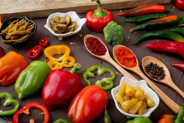 Close-up view of peppers with spices, broccoli, tomato on maroon surface