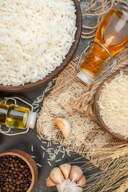 Close up view of perfect long rice brown bowls on nude color towel fallen oil bottles garlics peppers on dark background