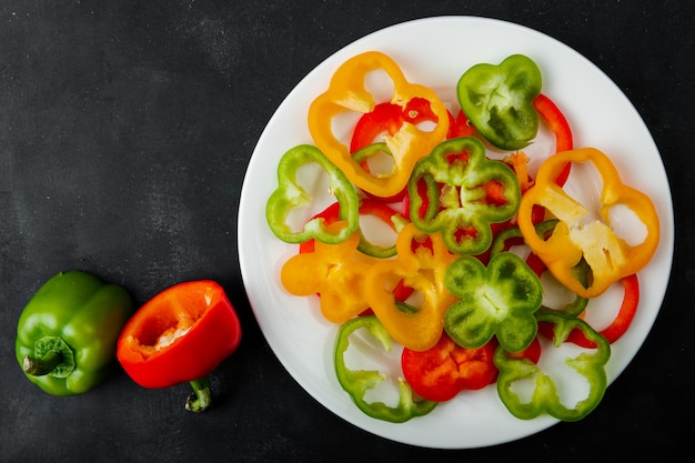 Close-up view of plate full of sliced peppers with whole and cut peppers on black background