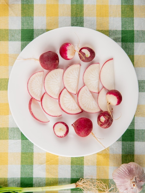 Free photo close-up view of plate full of whole and sliced radish with garlic on plaid cloth background