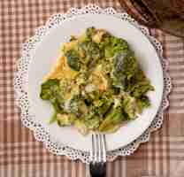 Foto gratuita vista del primo piano del piatto del pasto con le uova e broccoli e forcella sul centrino di carta sul fondo del panno del plaid