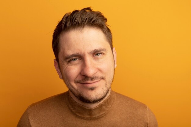 Close-up view of pleased young blonde handsome man looking  isolated on orange wall