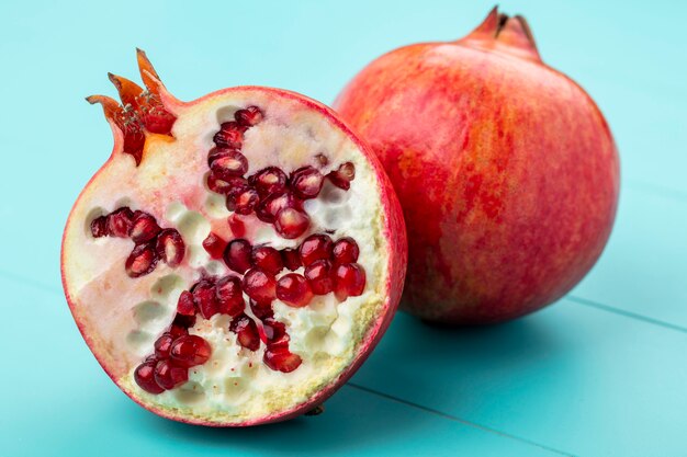 Close up view of pomegranate half with whole one on blue surface