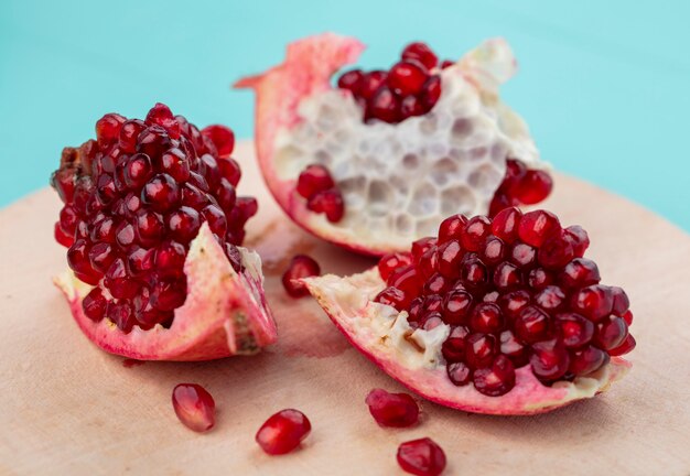 Close up view of pomegranate pieces and berries on cutting board on blue surface