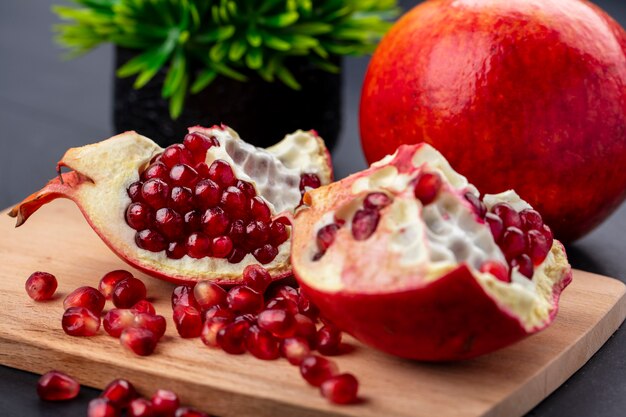 Close up view of pomegranate pieces and berries on cutting board with whole one on black surface