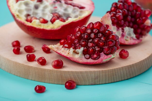 Close up view of pomegranate pieces and berries with pomegranate half on cutting board on blue surface
