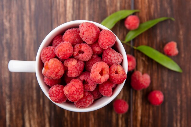 Close up view of raspberries in cup with leaves on wooden surface