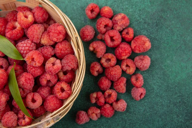 Close up view of raspberries with leaves in basket and on green surface