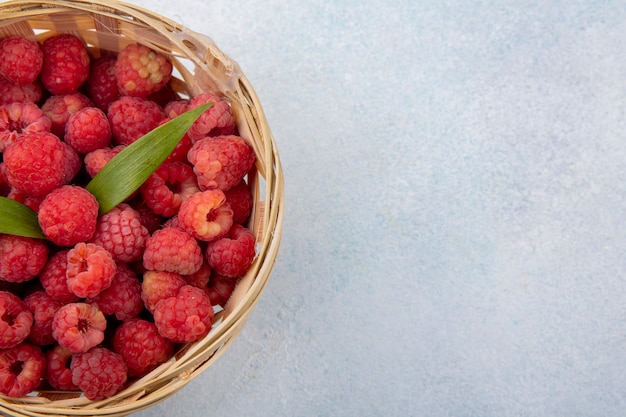 Close up view of raspberries with leaves in basket on white surface