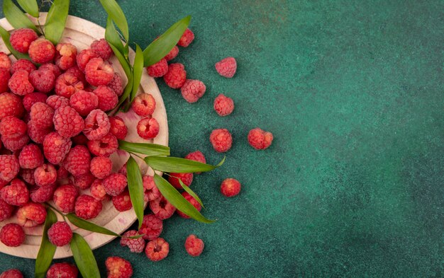Close up view of raspberries with leaves on cutting board on green surface