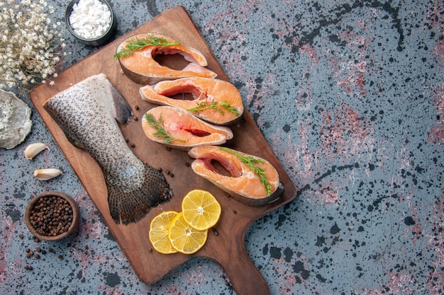 Close up view of raw fishes lemon slices greens pepper on wooden cutting board and flower on blue black colors table