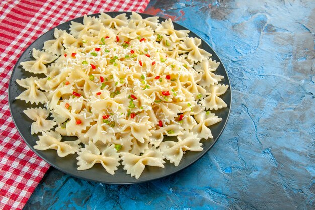 Close up view of raw Italian farfalle pasta on red stripped towel on the left side on blue background