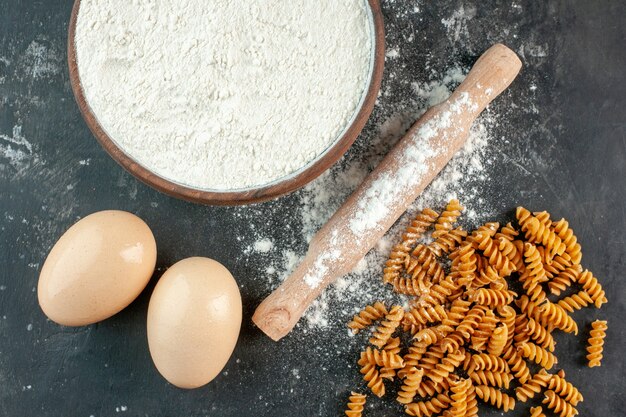 Close up view of raw Italian pastas two eggs and flour in a brown bowl rolling-pin on gray background