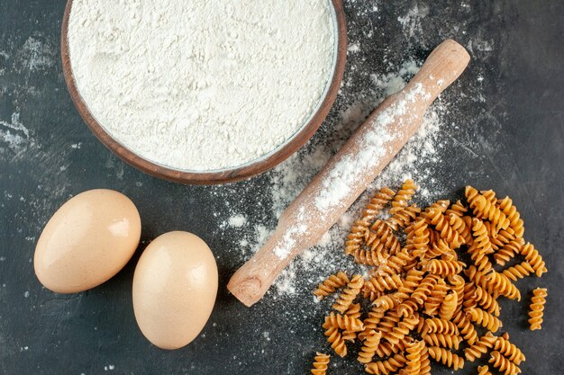 灰色の背景に茶色のボウル麺棒で生のイタリアンパスタ2個の卵と小麦粉のクローズアップビュー