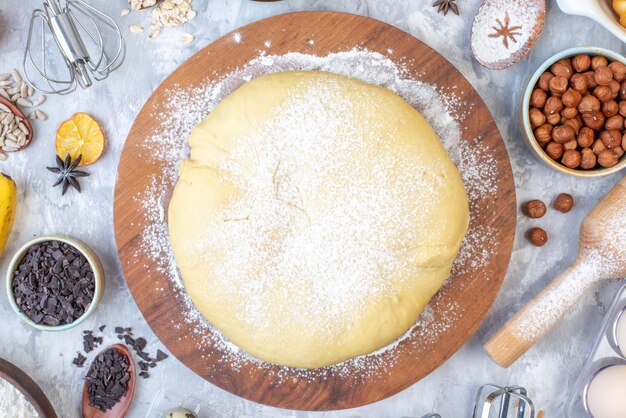 Close up view of raw pastry on round wooden board grater and set of foods on ice background