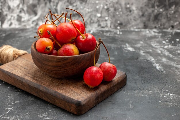 Close up view of red cheries in a brown bowl and on small cutting board on gray