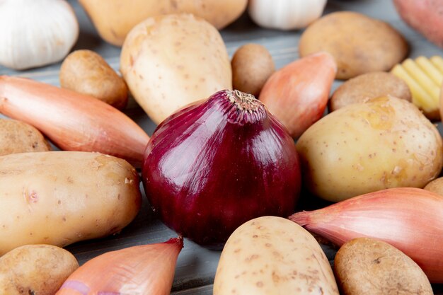 Close up view of red onion with shallots and potatoes around on wooden background