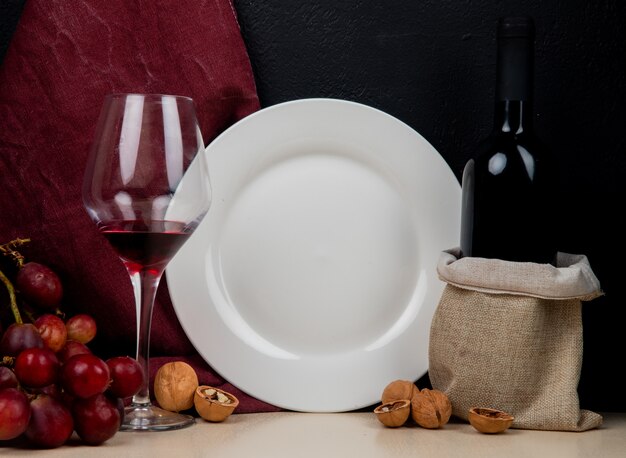 Close-up view of red wine and empty plate with grape and walnut on white surface and black background