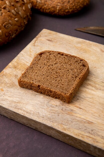Close-up view of rye bread slice on wooden surface and maroon background