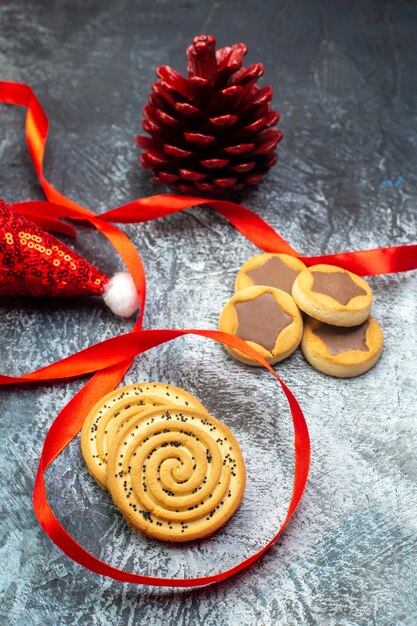 Close up view of santa claus hat red conifer cone and various cookies on dark surface