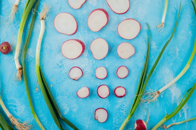 Close-up view of scallions with whole and sliced radishes on blue background