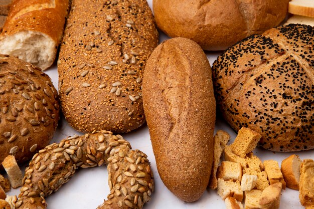 Close-up view of seeded baguette and bread pieces with bagel cobs on white background