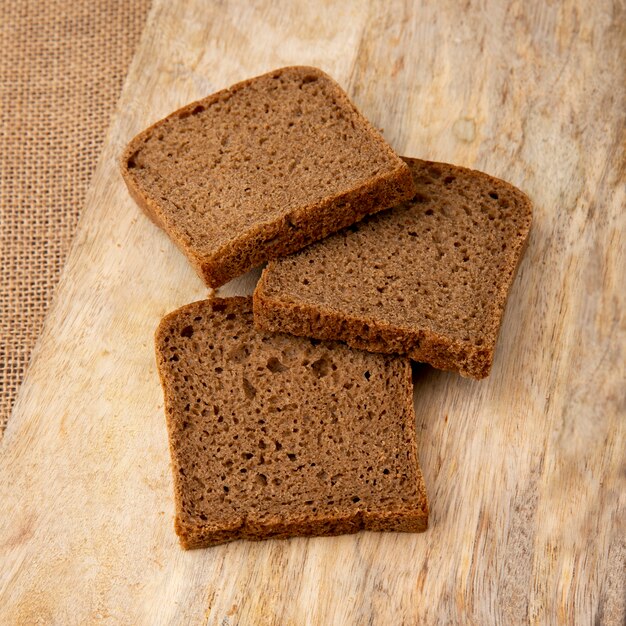 Close-up view of sliced black bread on wooden surface and sackcloth background