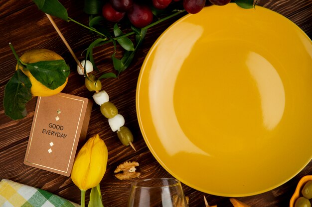 close-up view of sliced parmesan cheese with lemons olive walnut grape and empty plate on wooden background