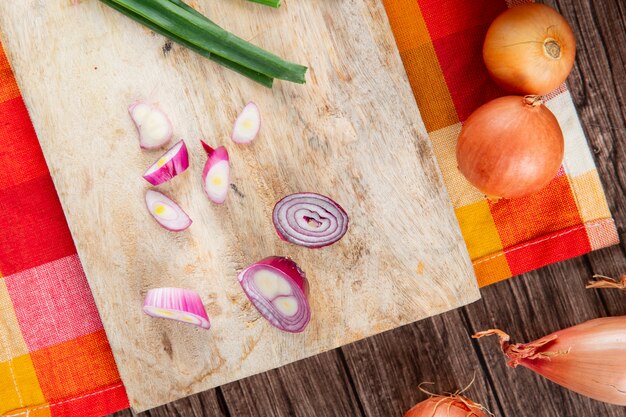 Close-up view of sliced red onion on wooden surface with yellow onions on wooden background