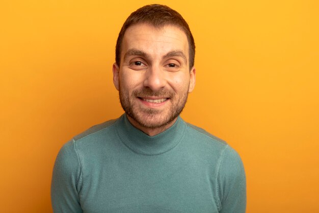 Крупным планом вид улыбающегося молодого кавказского человека, смотрящего в камеру, изолированную на оранжевом фоне