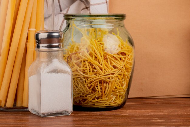 Close-up view of spaghetti pasta in jar and salt with bucatini pasta cloth and note pad on wooden surface