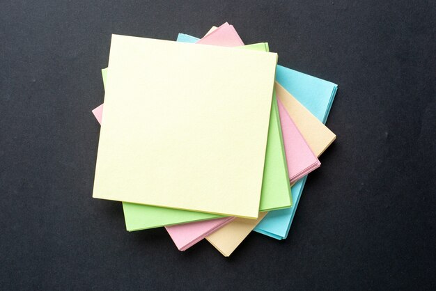 Close up view of stacked sticky coloured note cubes on isolated black wave background with free space