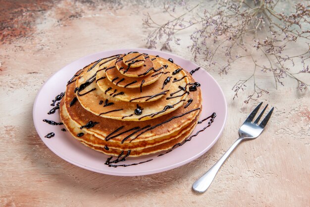 Close up view of stuffy pancakes decorated with chocolate syrup on a white