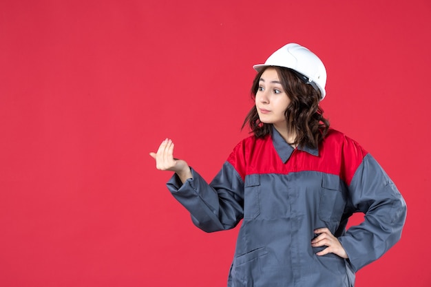 Close up view of surprised female builder in uniform with hard hat and calling someone on isolated red wall