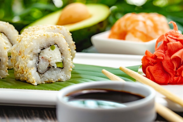 Close up view of sushi rolls with rice, shrimps, avocado and cream cheese with soy sauce on a bamboo leaves