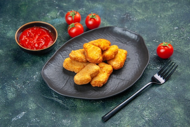 Close up view of tasty chicken nuggets in black plate tomatoes fork on dark surface with free space