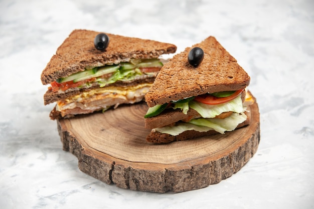 Close up view of tasty sandwich with black bread decorated with olive on a wooden cutting board on stained white surface with free space