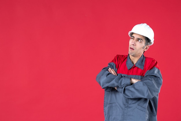 Close up view of thinking young architect in uniform with hard hat on isolated red wall