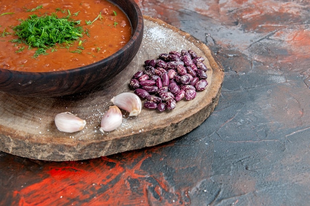 Close up view of tomato soup beans garlic on wooden cutting board on mix color table