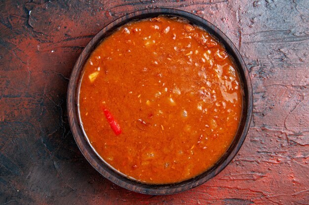 Close up view of tomato soup in a brown bowl on mixed color table