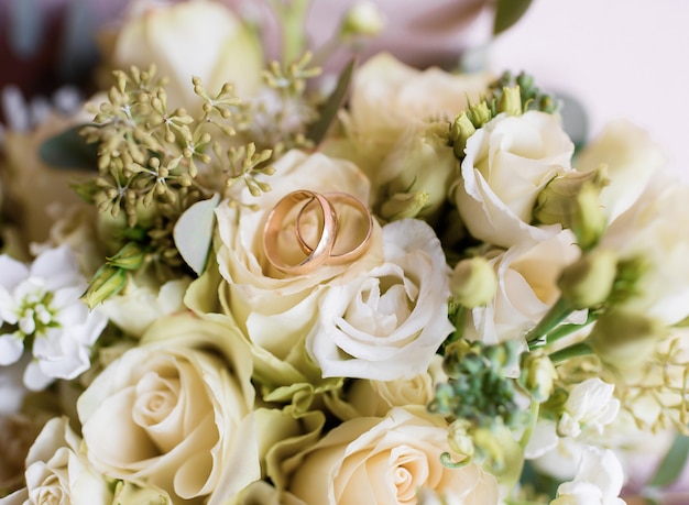 장미 꽃다발에 누워 있는 두 개의 금 결혼 반지의 클로즈업 보기