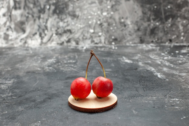 Close up view of two red cherries with green stem on gray