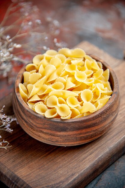 Close up view of uncooked pastas on wooden cutting board on mixed color table