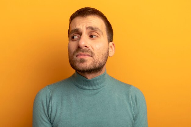 Close-up view of unpleased young caucasian man looking at side isolated on orange background with copy space