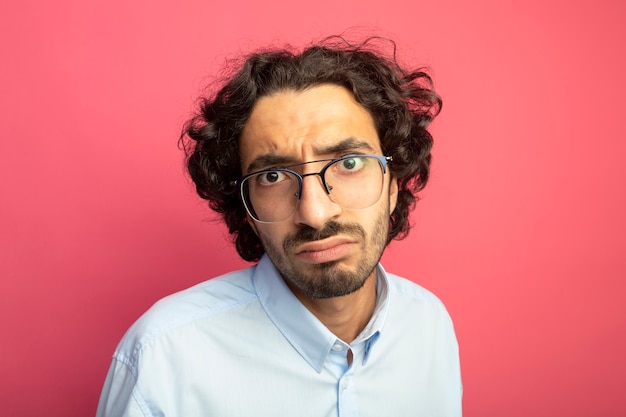 Close-up view of unpleased young handsome man wearing glasses looking at front isolated on pink wall